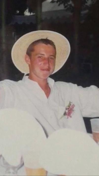 Young man wearing a white outfit and a wide brimmed white hat smiling to camera