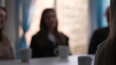 A blurred image of a girl with a mug on the table in front of her