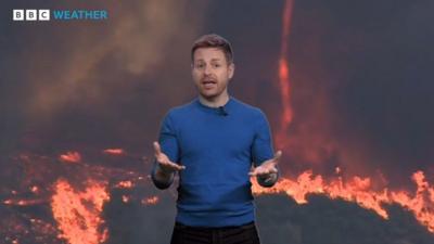 Tomasz Shafernaker stands in front of a picture of the ground on fire and a firenado