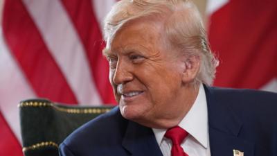 Donald Trump smiles in front of a US flag