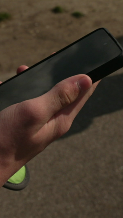 A person's hand with a smartphone outside a school gate.