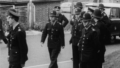 Several police officers in uniform with helmets parole the street.