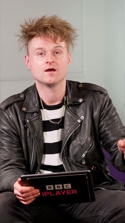 Aman with scruffy blonde hair, wearing a leather jacket over a black and white striped top.