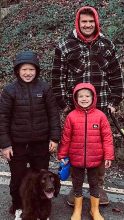 A man in a checked jacket with his sons who are in red and black puffer jackets