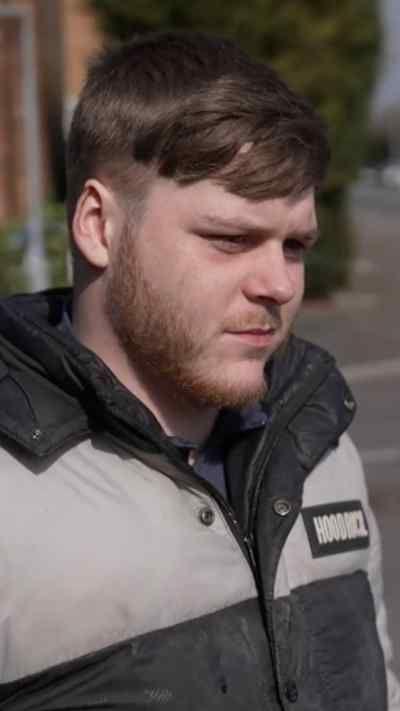 A man with short brown hair and a trimmed short beard wearing a gret and black jacket lays flowers.