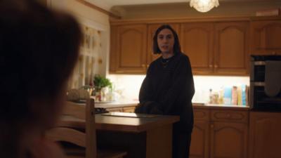 Young woman stands in a kitchen looking surprised 