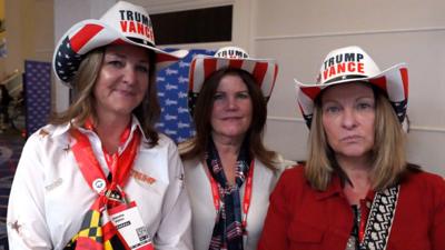 Three middle-aged women standing side by side wearing Trump Vance cowboy hats