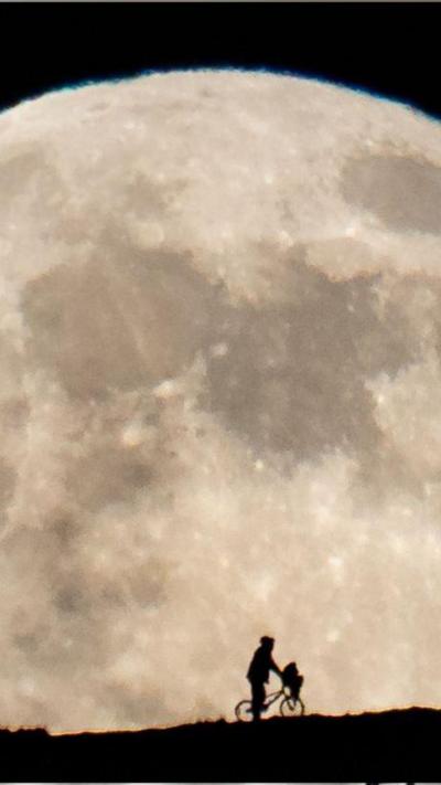 A silhouette of a man pushing a bike in front of the moon