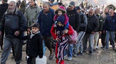 A child carries a water bottle and a woman carries another child, as part of a long queue of people