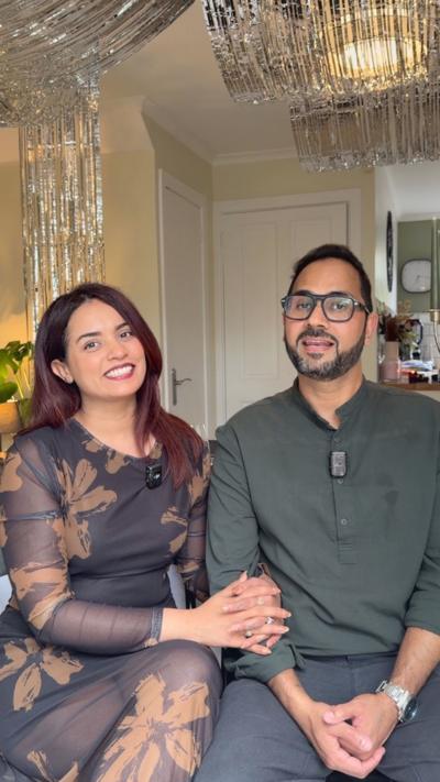 A man and a woman with their arms round each other, smiling at the camera. The woman is making a peace sign with her hand.