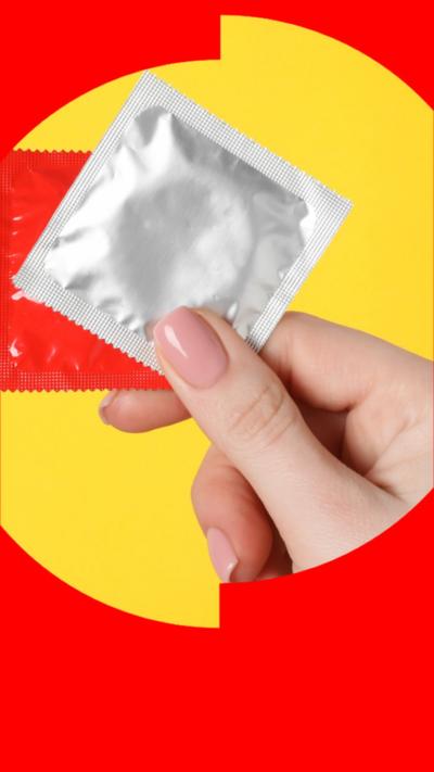 A woman's hand holding up a red and a silver condom packet, in front of a yellow background.