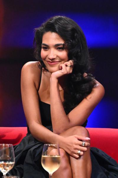 Olivia Dean in a black dress on a red sofa