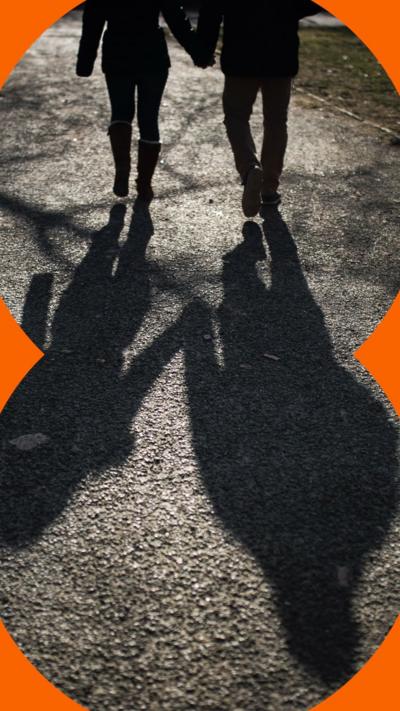 A couple on a walk holding hands are seen in silhouette. Their shadows stretch out long behind them.