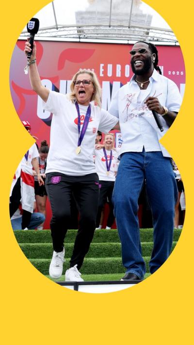 Sarina Wiegman and Burna Boy smile as they dance on stage at the Lionesses victory parade
