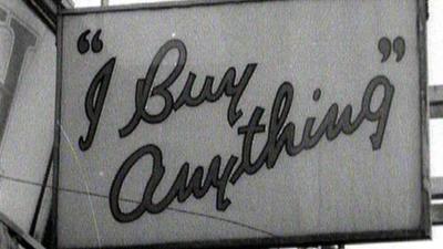 Black and white photograph of a sign on the side of a building that says "I Buy Anything"