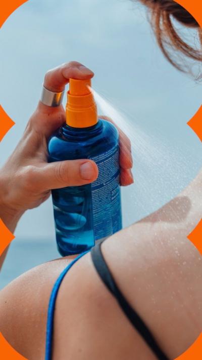 A woman spraying sunscreen on her shoulder, viewed from behind.