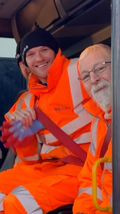 Three bin workers wearing orange hi-vis inside a bin wagon's cab