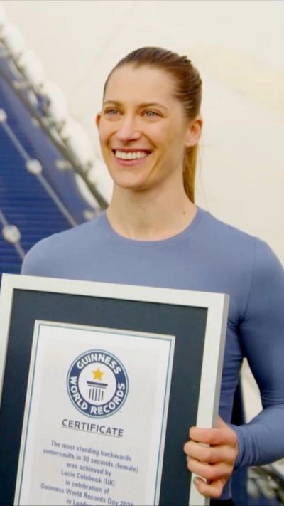 A woman with a blonde ponytail smiling and holding a certificate in a frame. She is wearing a blue top.