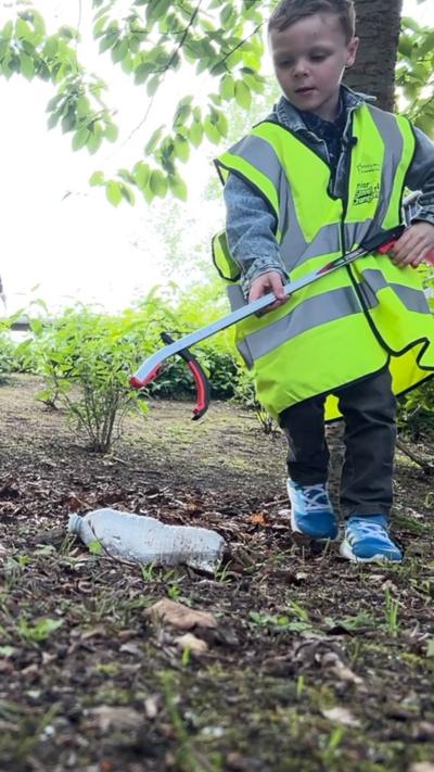 a little boy in a green hi vis jacket picking up litter with a litter picker