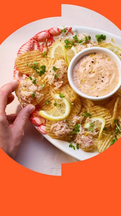 Crab loaded crisps on an oval shaped plate, with a round container of sauce in the middle