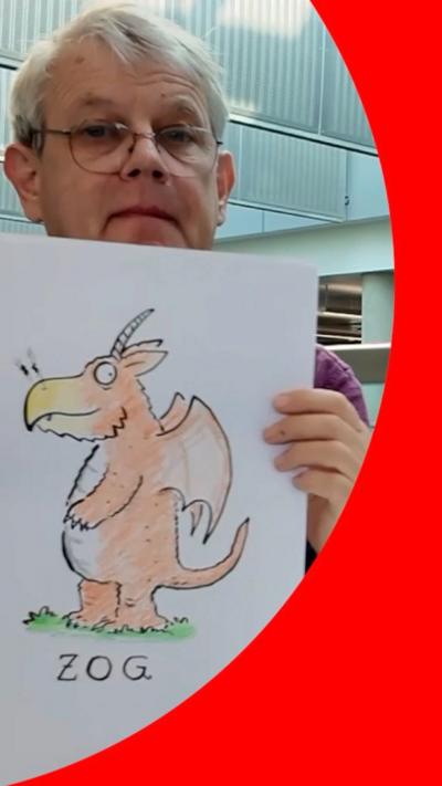Axel Scheffler, wearing a green jumper mid-drawing, in his studio. There are paint pots and brushes on his desk