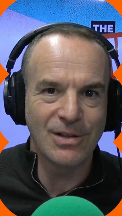 Martin Lewis wearing black headphones and zip top, sitting behind a green mic