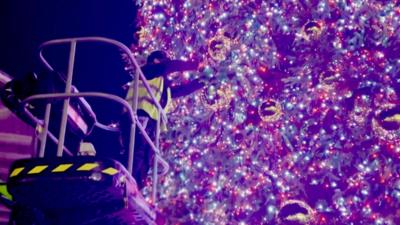 A man places the final gold bauble on the Covent Garden Christmas tree