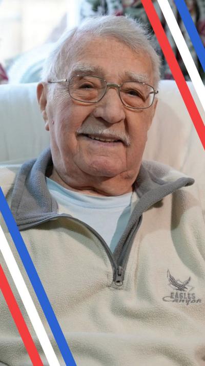 Jack Hearn sits in an armchair in his living room wearing a white jumper and glasses