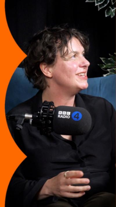 Woman with dark brown hair wearing a black shirt sat in front of a mic.