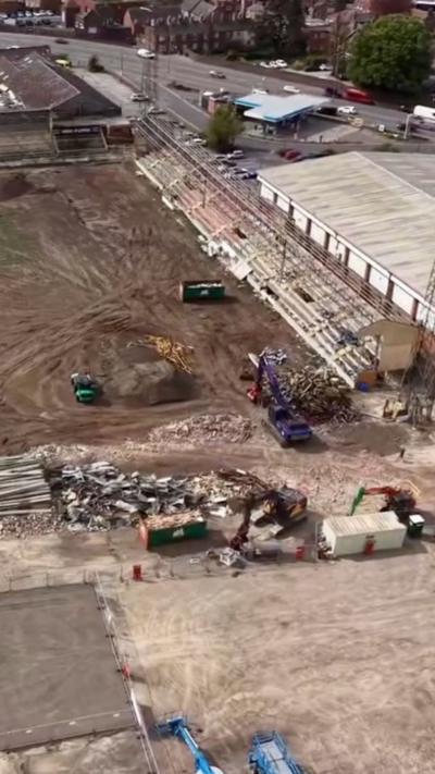 Drone photography shows old football ground being demolished, turf is all dug up and machinery present.