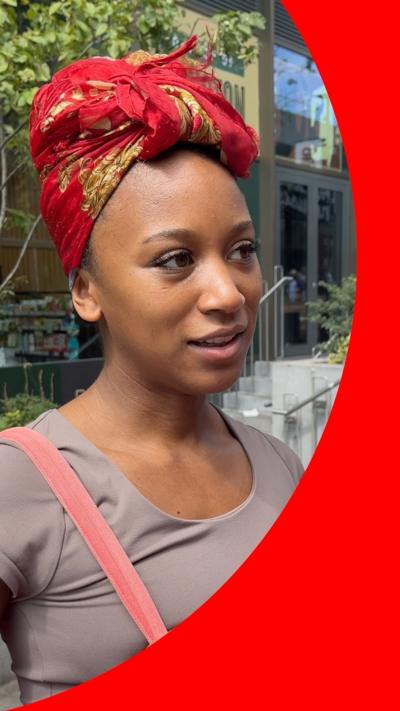 A woman standing in a street smiling. She is wearing a red headscarf.