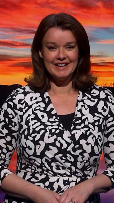 Weather presenter Gillian Smart smiles at the camera. She has mid-length brown hair and is wearing a black and white patterned dress. She is standing in front of a green screen that is showing a picture of Scotland.