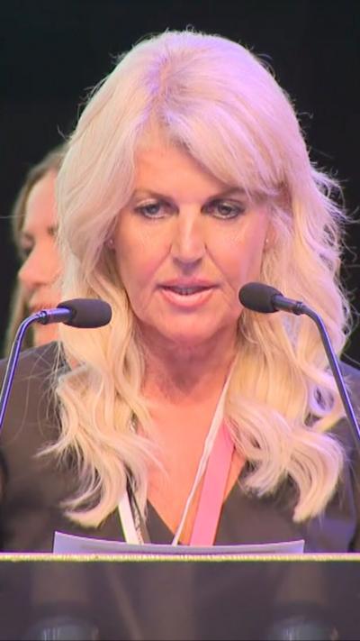 Woman with blonde hair and two microphones in front if her.