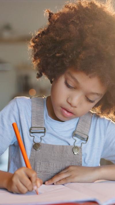 Young girl sits at table writing in a book