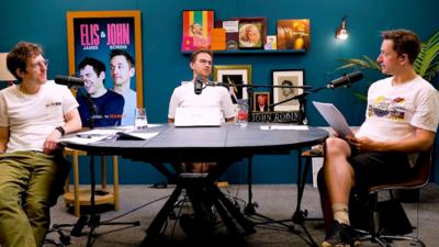 Elis & John in the podcast studio, sat around a table in front of microphones.