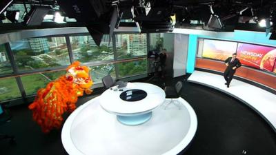 A Chinese lion dancing in the BBC's new Newsday studio in Singapore as presenter Rico Hizon dance nearby