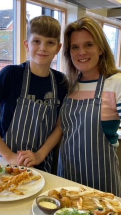 Boy and woman both wearing a stripey apron with food in front of them. 