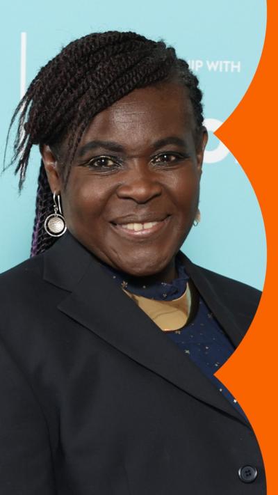 Dame Dr Maggie Aderin-Pocock poses for the camera. She has black braids and wears a dark blue suit jacket 