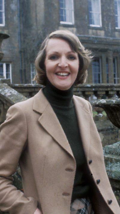 Penelope Keith standing on the steps of a country house