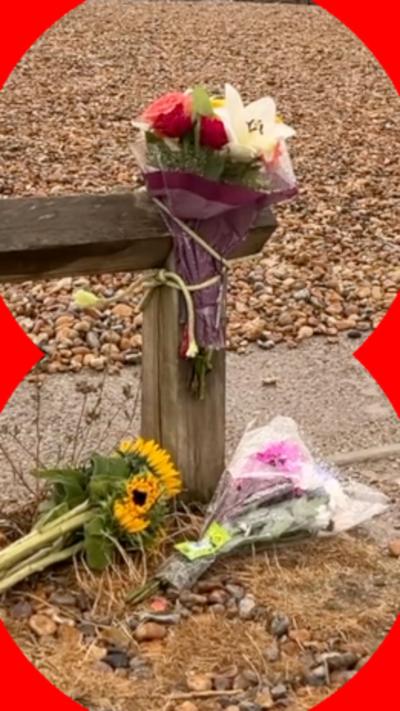 Flowers laid against a wooden post on a shingle beach.