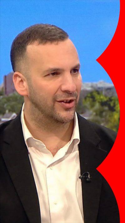 Zack Polanski has short brown hair and wears a black suit jacket and white shirt