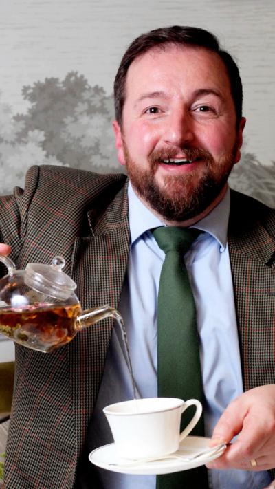 Man with brown hair and beard pouring tea from teapot into a cup