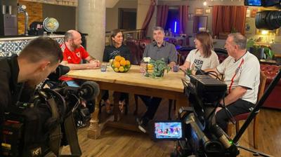 Football fans sit at a table being filmed