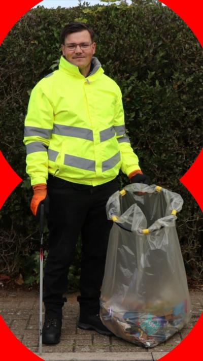 A man, Connor, stands on a pavement. He wears a hi-vis jacket and holds a litter picker and rubbish bag