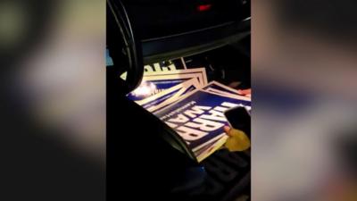 Harris/Walz campaign signs are seen being removed from a car boot.