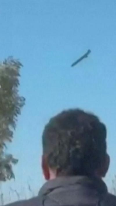 A drone falling through the sky. A man stands watching with his back to the camera