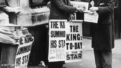 Newspaper stands reading "The King: To-Day" and "The King Summons His Staff".