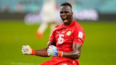 Edouard Mendy in red kit and white gloves screams in celebration while on his knees on a pitch 