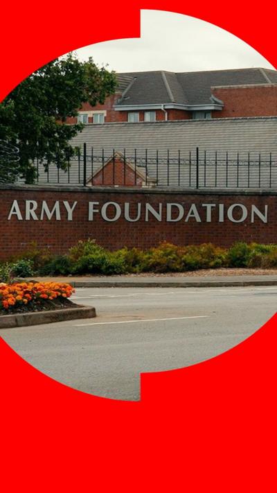 The words Army Foundation College are on a brick wall at the entrance to the campus. Large black gates are open with a red and white barrier slightly beyond. The college's buildings are behind. 