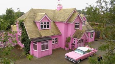 Huge pink house with pink cadillac parked in front